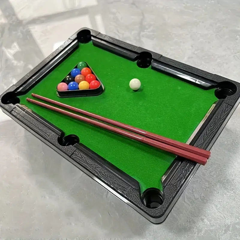 Miniature pool table with balls and cues on a gray surface